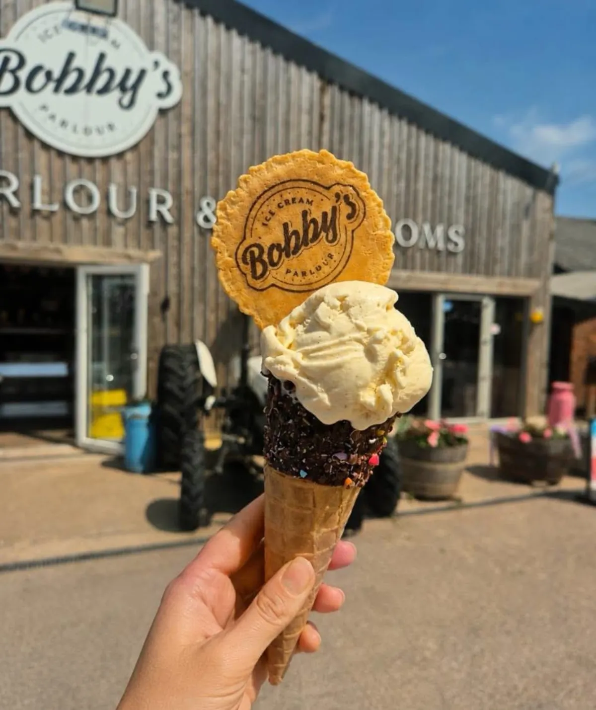 A vanilla cone with a Bobby's wafer held up outside the parlour